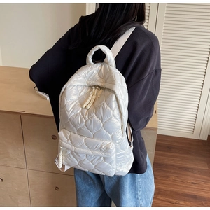 Detailed back view of a white quilted puffer backpack with woven zipper pulls on a model
