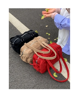 Trois sacs Boston en daim noir, kaki et rouge avec détails de nœuds sur fond de rue pavée