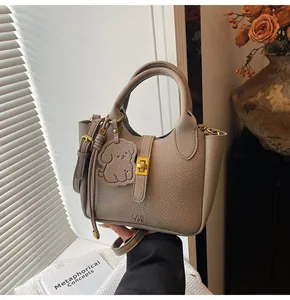 Detail of taupe lychee texture handbag with gold twist lock and dog charm on table