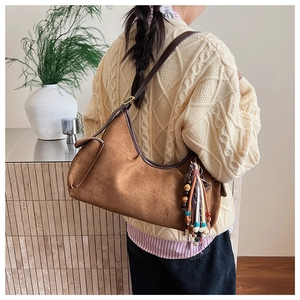 Detailansicht einer braunen Wildleder-Hobo-Tasche mit Perlenanhänger am Modell