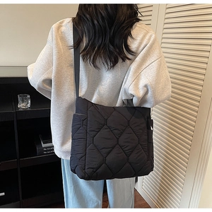 Close-up of black quilted tote bag with rhombus pattern and wide fabric shoulder strap