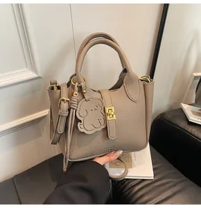 Detail of lychee textured leather bucket bag with puppy charm and golden rotary lock