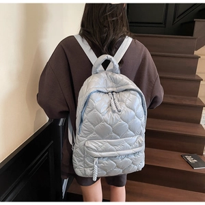 Detail of light blue quilted nylon backpack with padded texture and front zip pocket