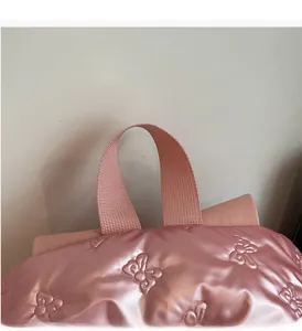 Detail of pink padded backpack with embossed butterfly patterns and sturdy top handle