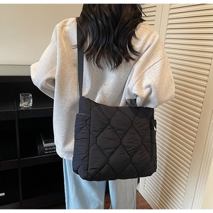 Detail of black quilted puffer tote bag with diamond pattern and wide shoulder strap