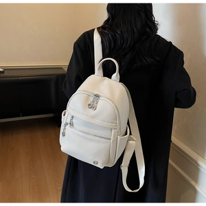 Detail view of a white pebbled leather fashion backpack on model with silver zippers