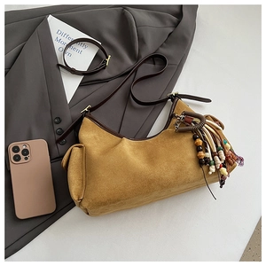 Détail du sac hobo en daim moutarde avec pompons bohèmes et bandoulière en cuir