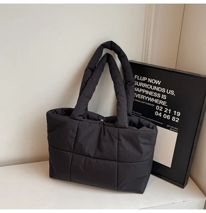 Dettaglio della borsa tote trapuntata nera con ampi manici su uno sfondo minimalista