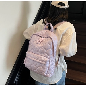 Detailed view of light purple quilted backpack with heart patterns worn on model's back