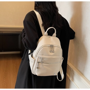 Close-up of cream-white backpack with pebble leather texture and metal ring zippers