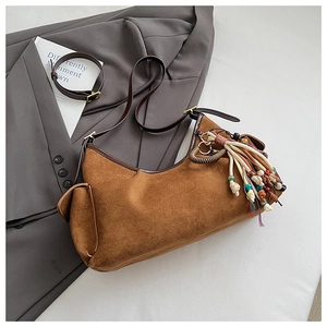 Detail der braunen Wildledertasche mit Lederriemen und buntem Quastenanhänger