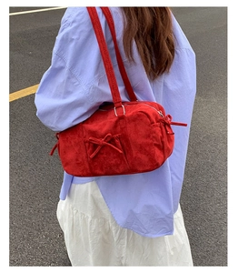 Détail du sac bandoulière en daim rouge avec un nœud élégant et fermeture éclair en métal
