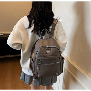 Rear view of a model wearing a taupe pebble leather backpack in a minimalist indoor setting