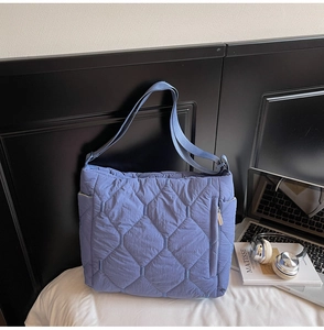 Detail of blue quilted tote bag showing hexagonal texture and side zipper pocket