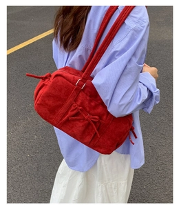 Sac à épaule en daim rouge avec nœud décoratif présenté dans un cadre minimaliste