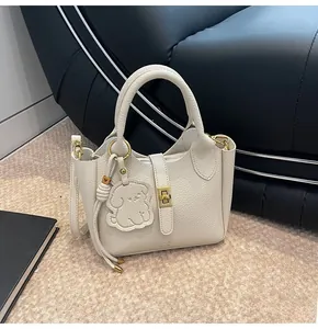Detail of off-white lychee grain leather handbag with gold buckle and puppy charm