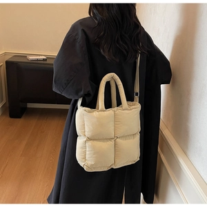 Model wearing a beige quilted puffer tote bag with cross-stitch design and adjustable strap