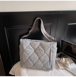 Detail of grey quilted tote bag featuring a vertical metal zipper pocket and wide strap