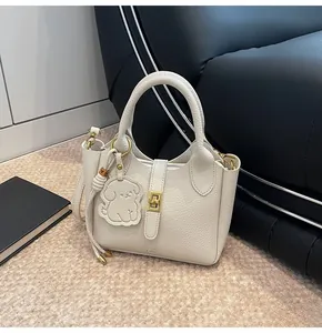 Close-up of beige lychee grain leather bucket bag with gold lock and puppy charm