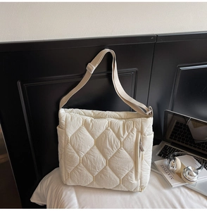 Close-up of quilted off-white tote bag with adjustable strap and side zipper detail