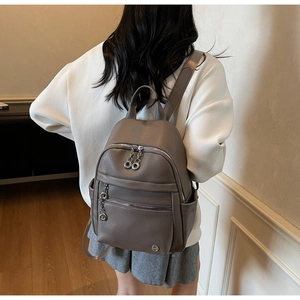 Detail of dark grey textured leather backpack featuring circular metal zipper pulls