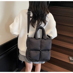 Model wearing a black quilted puffer tote bag with adjustable nylon crossbody shoulder strap