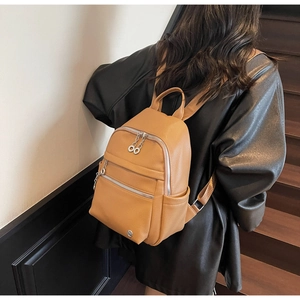 Detail of camel lychee pattern backpack showing silver zippers and decorative circle pendant