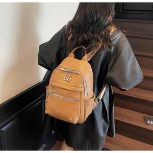 Detail of camel brown leather backpack featuring silver zippers and side pockets on a model