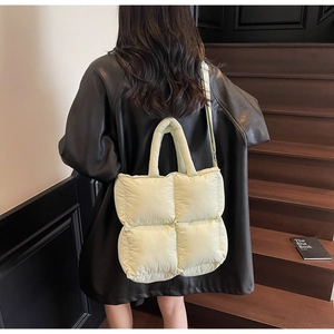 Detail of pale yellow quilted puffer tote bag on outdoor stairs with a black leather jacket