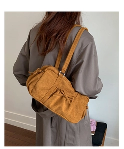 Détail du sac bandoulière en daim caramel avec nœud décoratif et texture plissée latérale