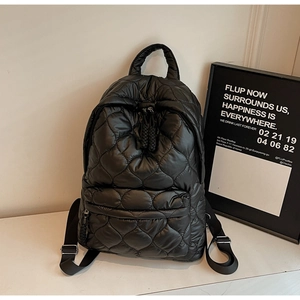 Detail of the black quilted puffer backpack showing diamond stitching and front zipper pocket