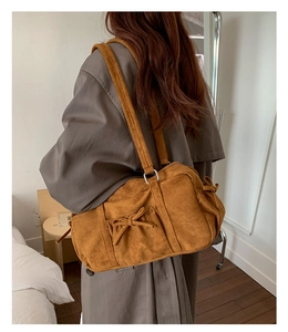 Détail du sac bowling en daim marron avec un nœud élégant sur la bandoulière latérale