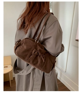 Détail du sac bowling en daim marron foncé avec un nœud décoratif et une bandoulière