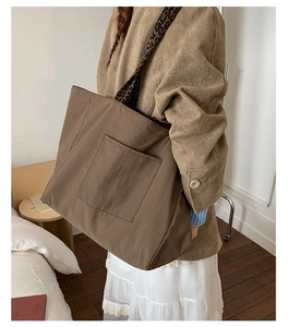 Detail of a large brown tote bag with leopard print strap and exterior pocket in home setting