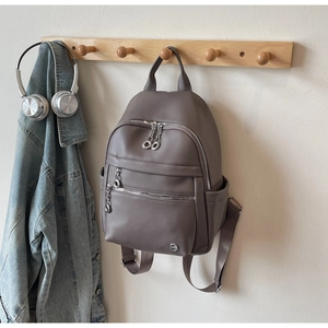 Detail of taupe leather backpack featuring litchi grain texture and silver ring zippers