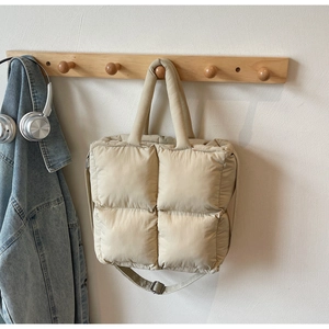 Detailed view of beige quilted tote bag on wooden rack with adjustable strap and puffy texture