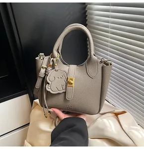 Detailed view of grey lychee leather bucket bag with gold clasp and dog charm accessory