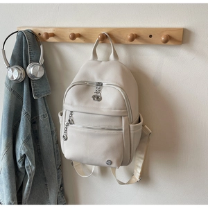 Detail of cream pebbled leather backpack with silver chain zippers and metal logo