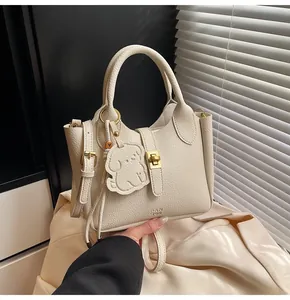 Detail of cream lychee texture leather handbag with gold hardware and dog charm