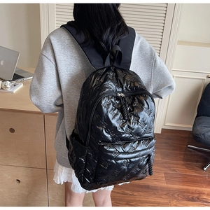 Detail of glossy black quilted backpack with embossed 3D bow patterns and zip cords
