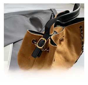 Detail of brown quilted bucket bag with golden hardware and chain strap on grey fabric