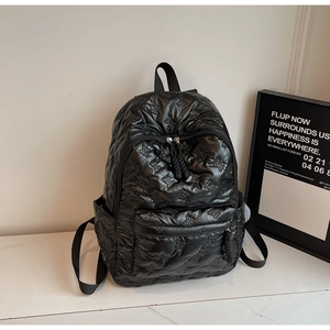 Detail of black quilted backpack featuring 3D bow patterns and high-gloss nylon texture
