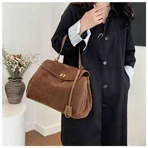 Detail of a brown suede handbag with a golden twist lock and elegant accordion pleats