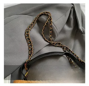 Detail of brown suede bucket bag featuring black leather handles and gold chain strap
