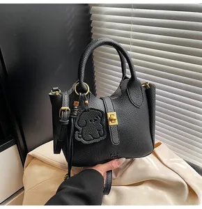 Detail of black lychee leather bucket bag featuring a dog charm and golden twist lock