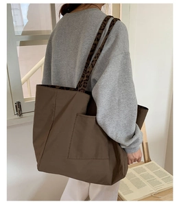 Close-up of brown tote bag featuring leopard print straps and front pocket detail