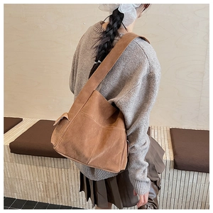 Détail d'un sac à bandoulière en daim marron avec poche latérale porté par modèle