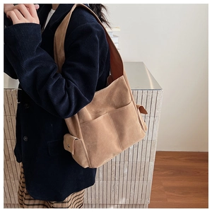 Détail d'un sac à bandoulière en daim marron montrant les poches et la sangle large
