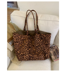 Detail of leopard print canvas tote bag leaning on white sofa with books and blanket
