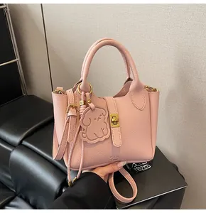 Detail view of pink lychee leather bucket bag with golden buckle and bear charm